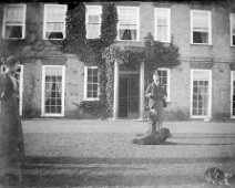 Father with dog & cat on lawn. Girl watching Sedgeford Hall Original caption: Father with dog and cat on lawn. Girl watching